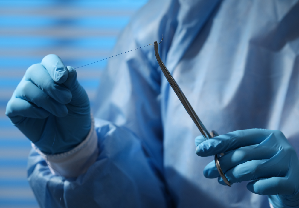 Médico segurando uma pinça e uma linha de sutura